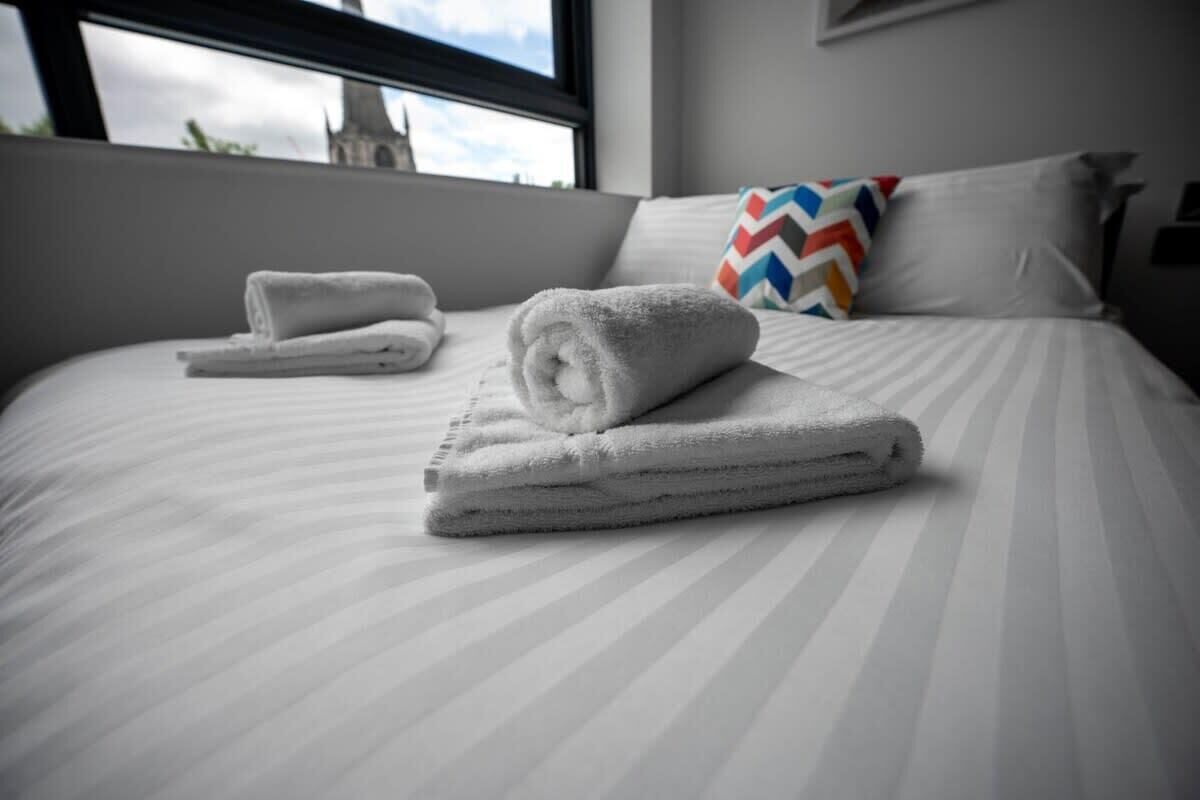 Un lit bien fait, avec des serviettes pliées, un coussin à motifs en chevrons et une vue sur la fenêtre.