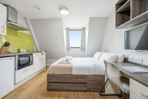 A modern hotel room with a kitchenette, a bed with white bedding, a desk with a chair, and a television. - Central Nottingham Cosy Budget Double Studio (Nottingham)