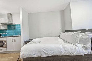 A bedroom with a bed, white bedding, a wooden headboard, a kitchenette with a microwave, and a blue-tiled backsplash. - Bright Budget Double Studio – Heart of Nottingham (Nottingham)