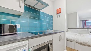 Una kitchenette compacta equipada con microondas, tostadora y horno, un lavamanos y una cama con ropa blanca.