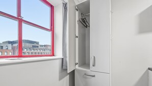 Habitación con ventana, armario blanco y vista a edificios.