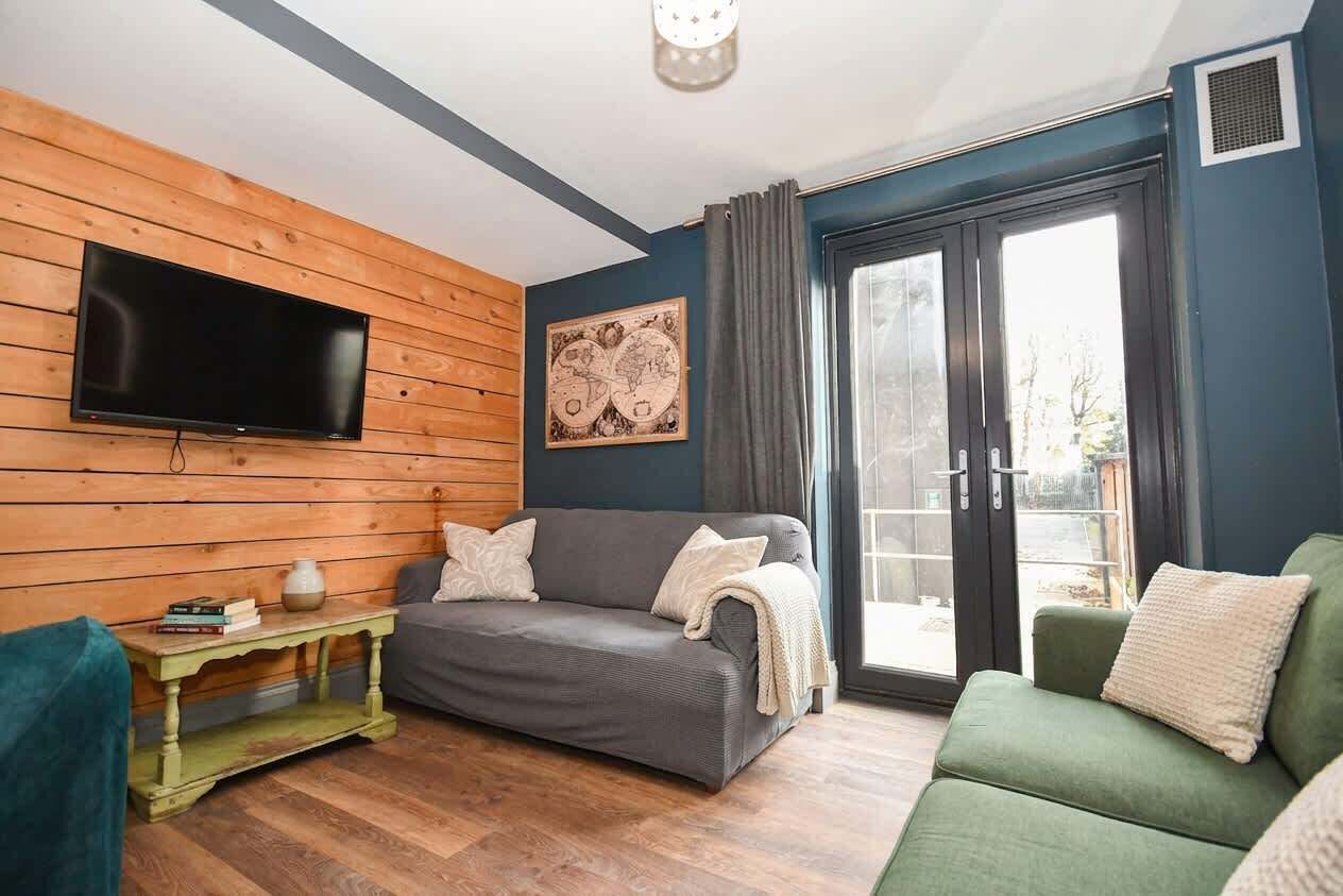 Un soggiorno con una TV a schermo piatto, una parete in legno, un divano verde e uno grigio, e una porta scorrevole in vetro.