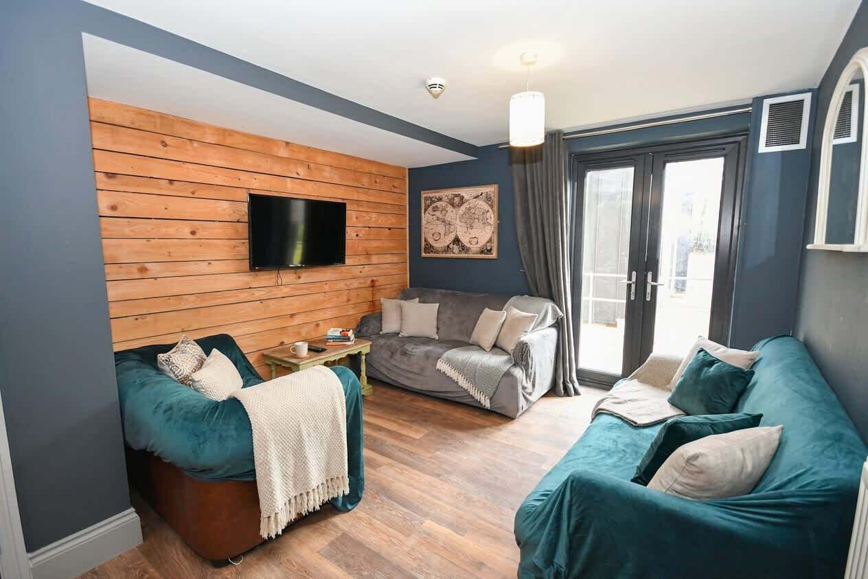 Una sala de estar acogedora con una pared de madera, un televisor de pantalla plana, dos sofás color turquesa y un sofá gris.