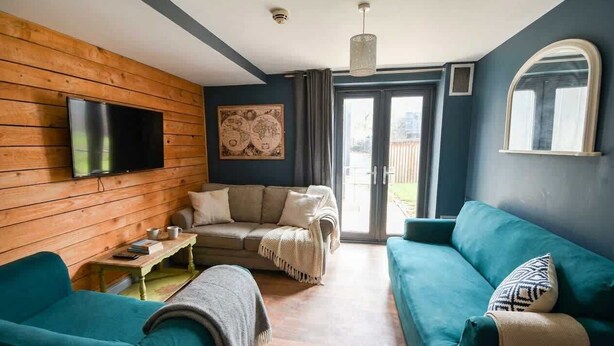 Un salon avec un mur en bois, un téléviseur, un canapé, une table basse et une porte-fenêtre coulissante donnant sur l’extérieur.