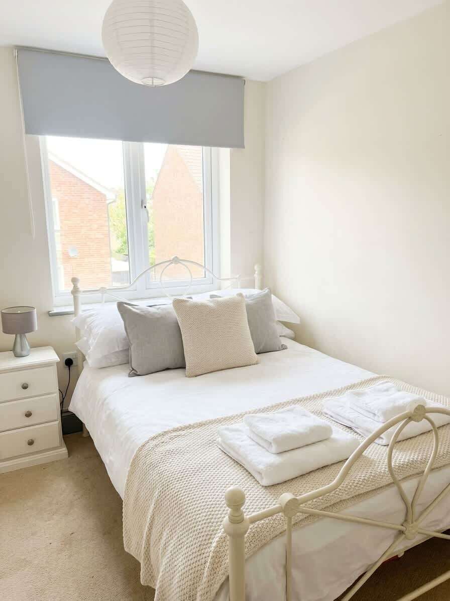 Une chambre à coucher avec un lit, une table de chevet, une lampe et une fenêtre donnant sur des immeubles.