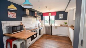 Une cuisine moderne avec des meubles blancs, un plan de travail en bois, un four à micro-ondes et un store rouge.