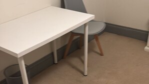 Ein weißer Tisch mit Metallbeinen, ein grauer Stuhl und ein Teppichboden.