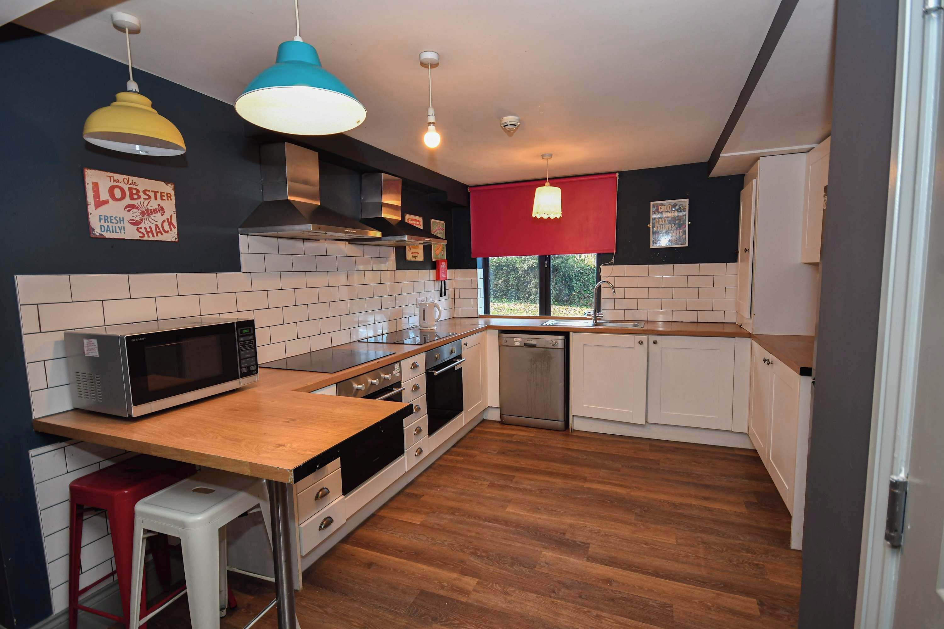 Une cuisine moderne avec des meubles blancs, un plan de travail en bois, un four à micro-ondes et un store rouge.