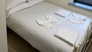 Ein Einzelbett mit weißer Bettwäsche, zwei Kissen und einem Fenster mit Jalousie.