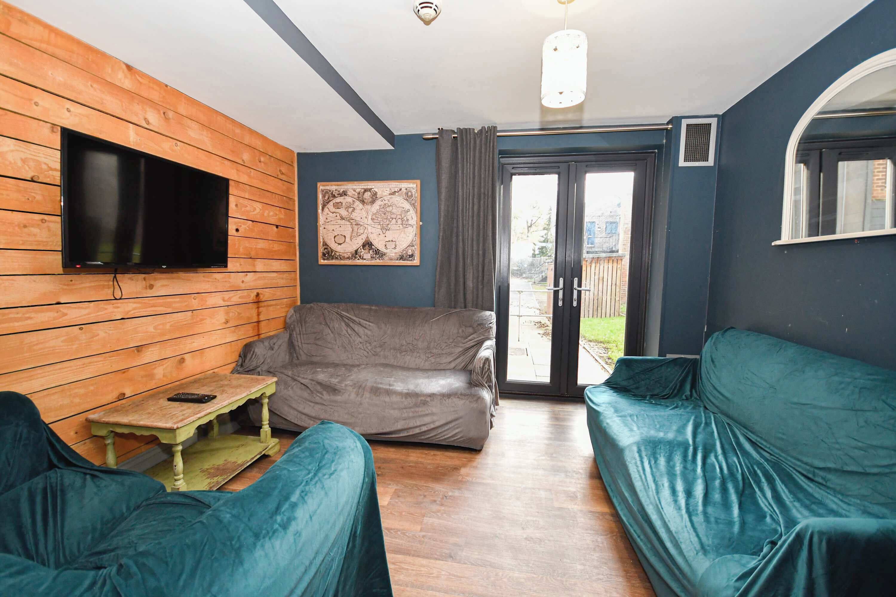 A cozy living room with a wooden wall, a flat-screen TV, a grey sofa, and teal armchairs.