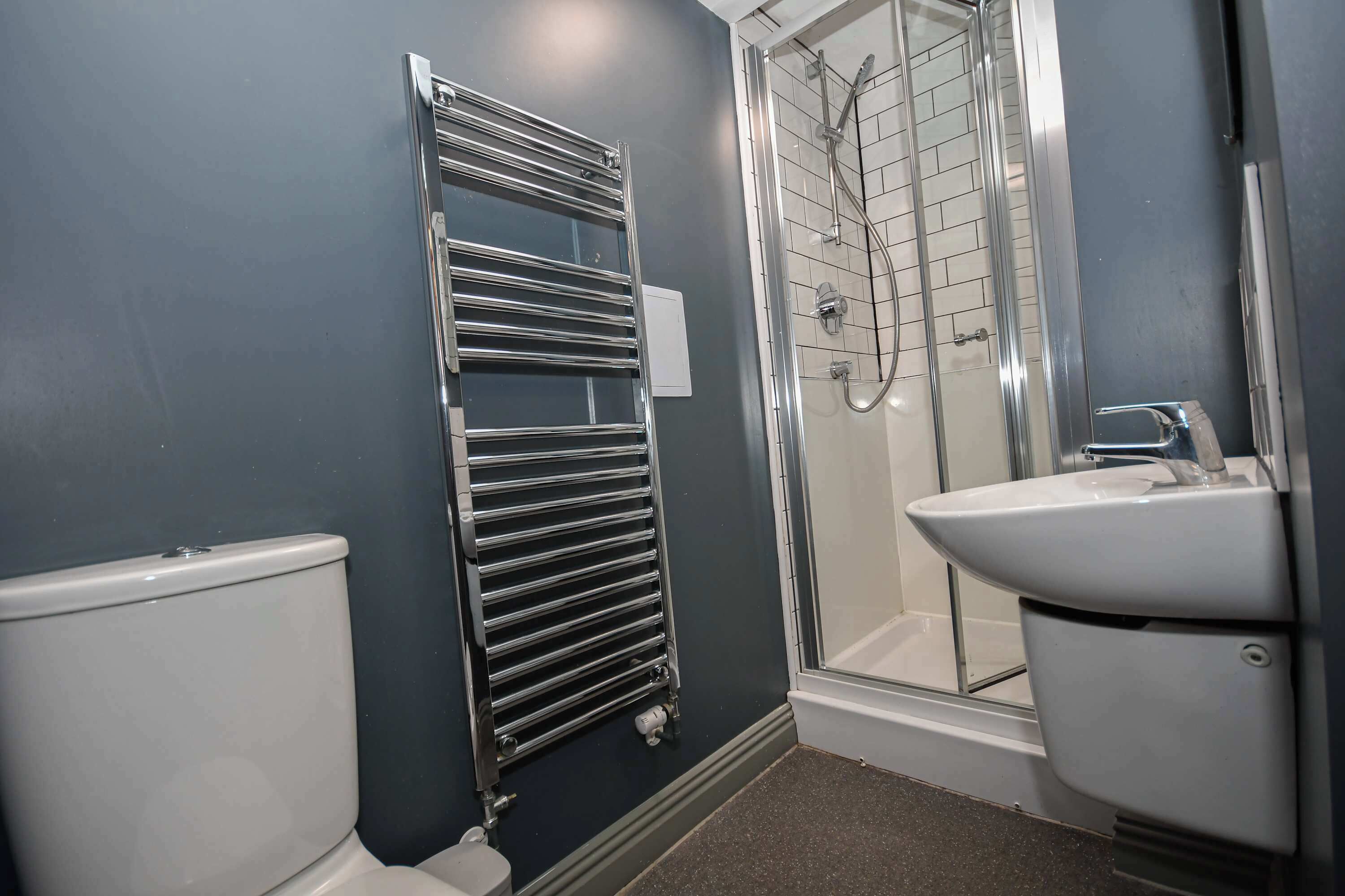 A bathroom with a toilet, a towel rack, a shower with a glass door, and a sink.