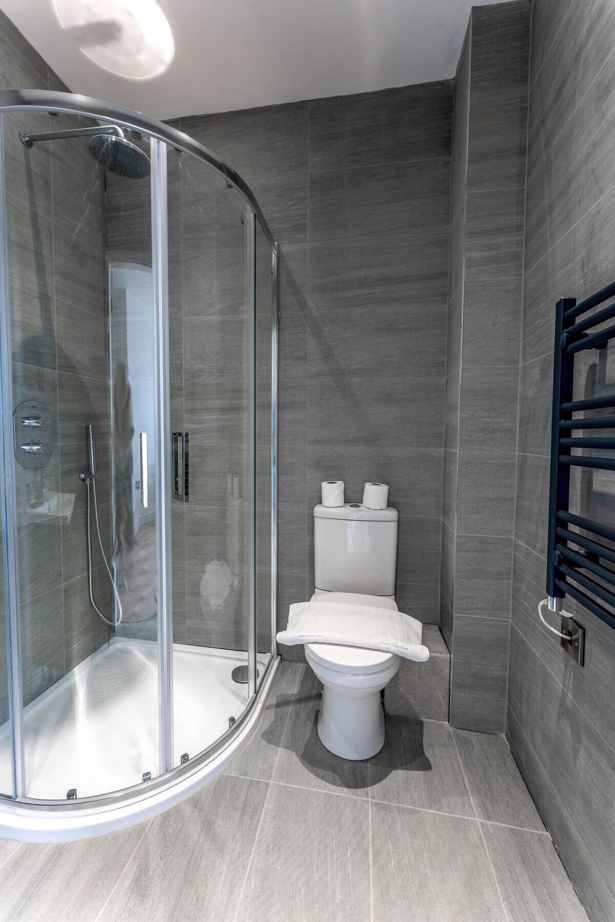 Een moderne badkamer met een douchecabine van glas, een toilet en een handdoekrek.