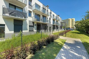 A multi-story residential building with balconies, a paved walkway, and a fence.