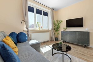 Ein Wohnzimmer mit Sofa, Couchtisch, Fernseher und einem Fenster mit Jalousien.