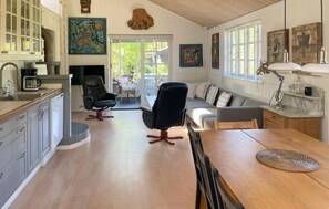 A spacious living area with a wooden dining table, a black office chair, a grey sofa, and a kitchen area with white cabinets and a coffee machine. - Stunning home in Vig with WiFi (Vig)