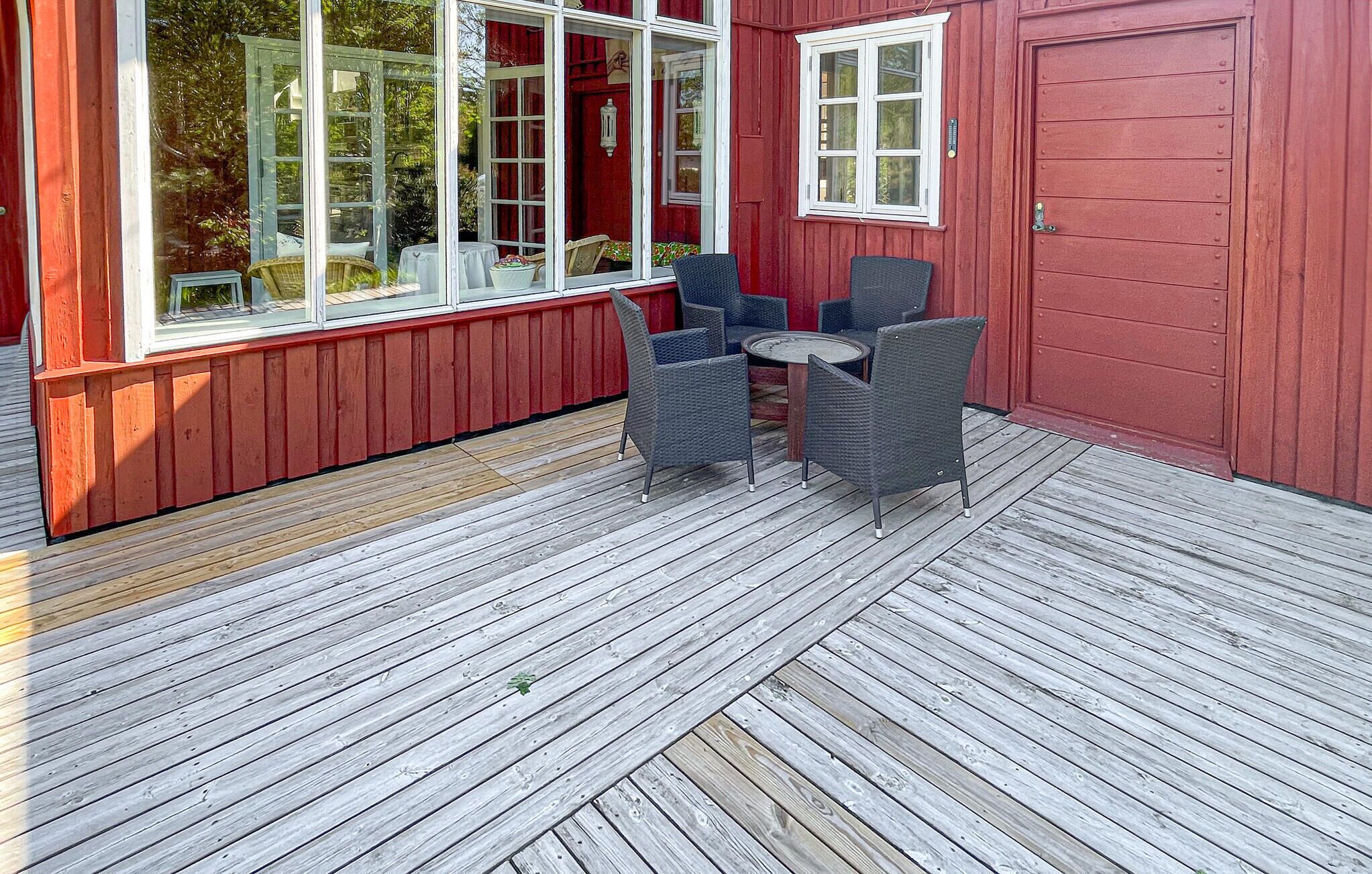 A wooden deck with a red building, two wicker chairs, and a small round table.