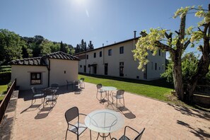A patio with outdoor seating, a white building with multiple windows, and a tree with white blossoms. - Villa Tegolato (Barberino Tavarnelle)