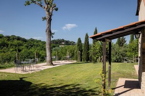Un patio con mobiliario exterior, una pérgola y vistas a un paisaje verde y exuberante.