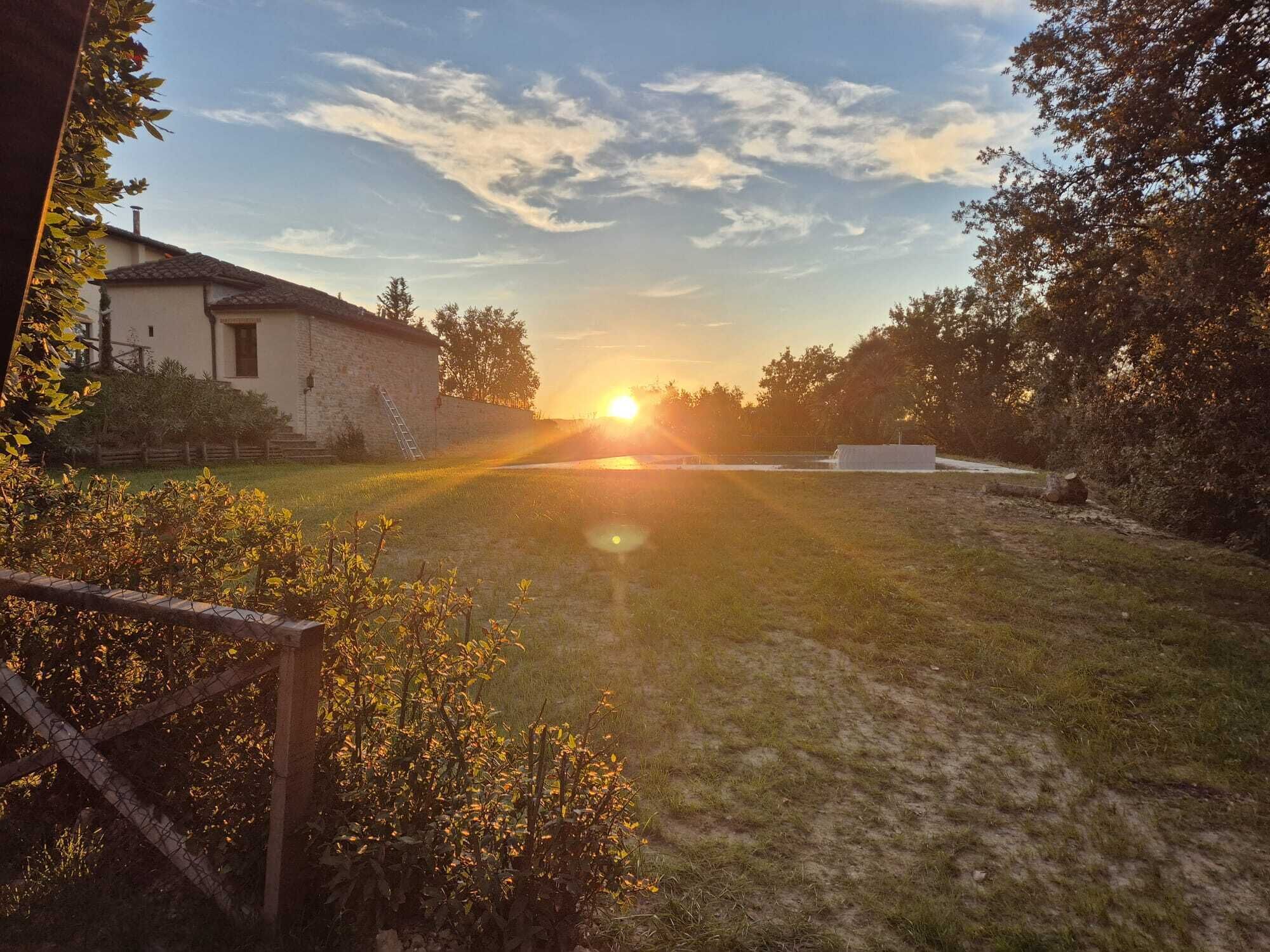 Ländliche Landschaft mit einem Haus, blauem Himmel und untergehender Sonne in der Ferne.