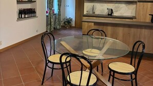 A dining area with a glass table and four chairs, a kitchen with modern appliances, and a brick ceiling. - Cascina Lungamerenda - Relax in Monferrato (Costigliole d'Asti)
