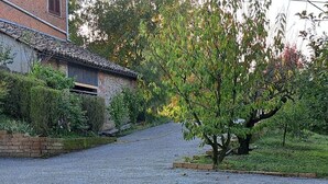 A gravel driveway leading to a brick house with a tiled roof, surrounded by greenery. - Cascina Lungamerenda - Relax in Monferrato (Costigliole d'Asti)