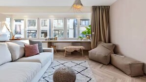 Ein modernes Wohnzimmer mit Sofa, Hocker und Blick auf die Stadt durch große Fenster.