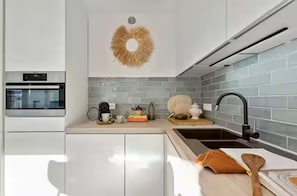 A modern kitchen with white cabinets, a built-in oven, a sink with a faucet, and a decorative wall piece. - Michelle | Stylish Renovated Apartment in the Heart of Ostend | Sleeps 8 (Oostende)