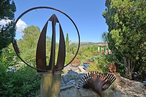 Eine Metallskulptur in einem Garten mit Blick auf ein Gebäude im Hintergrund.