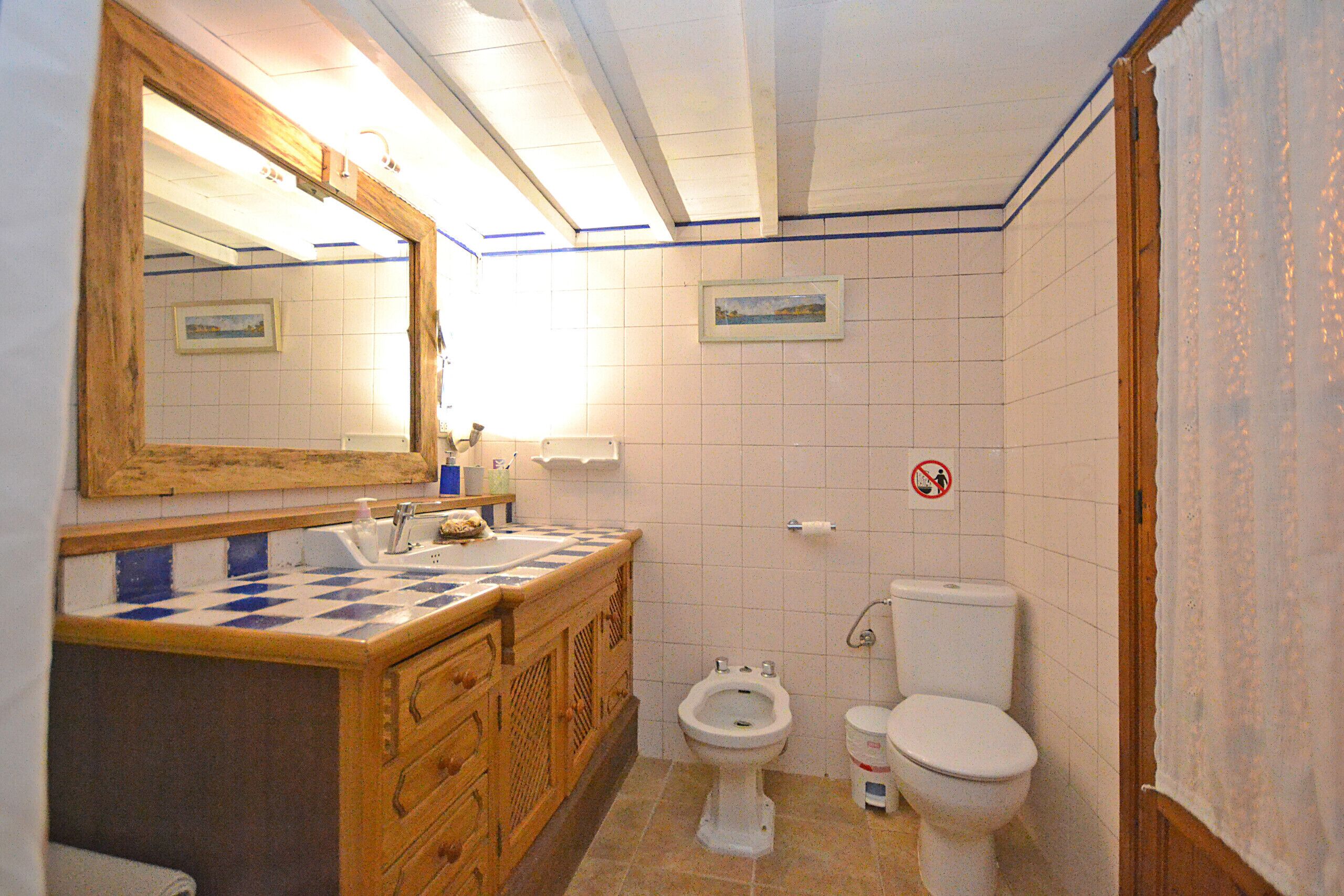 A bathroom with a wooden vanity, a sink, a mirror, a bidet, and a toilet.