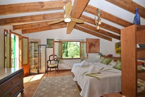 Ein Schlafzimmer mit Holzbalken, Deckenventilator, Bett mit grünen Kissen, Stuhl und Kommode.