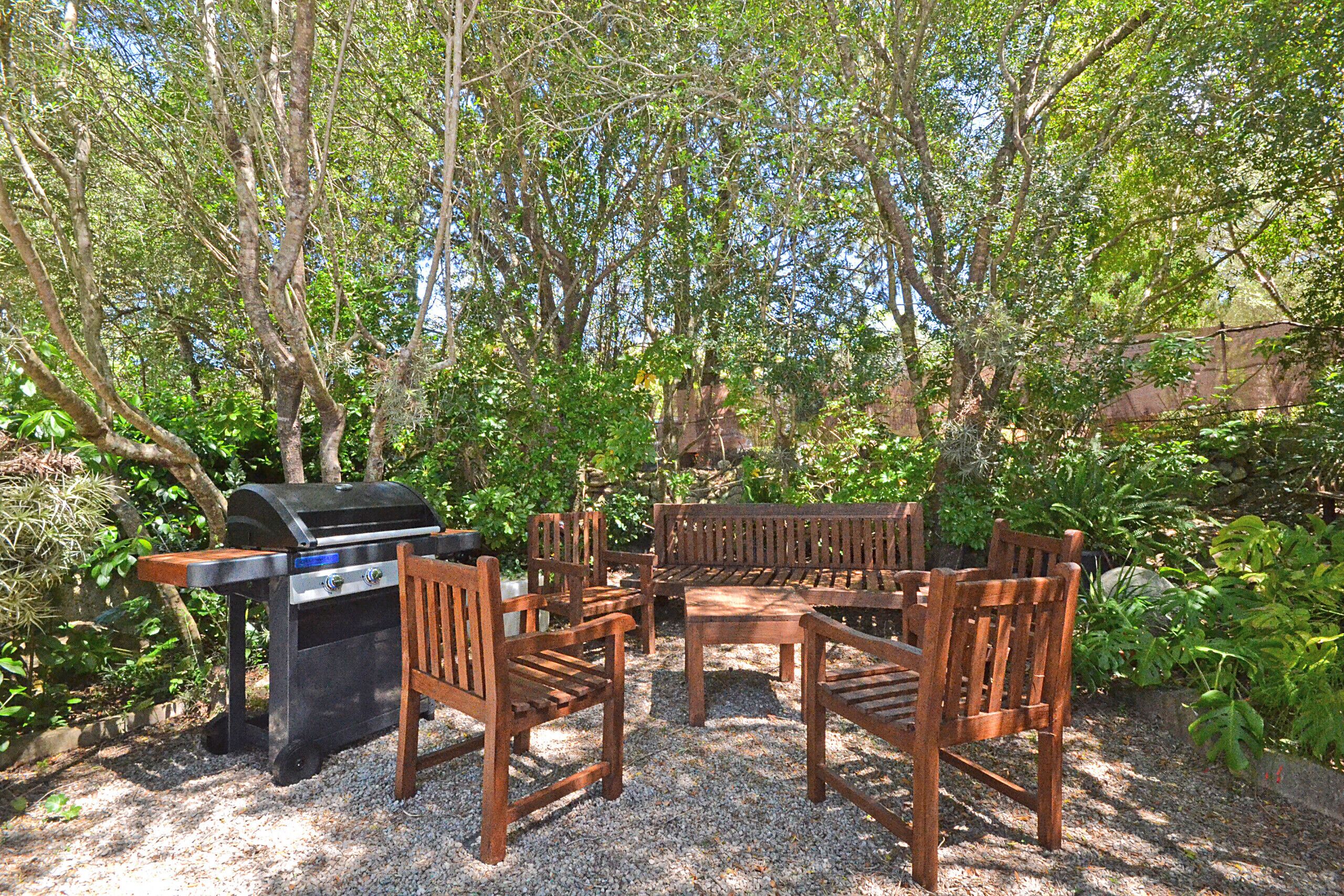 An outdoor seating area with a grill, surrounded by trees and plants.