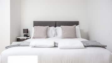 A neatly made bed with a grey headboard, white bedding, and a bedside table with a lamp.