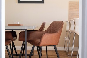 A dining area with a table and chairs, a framed picture on the wall, and a wooden floor.
