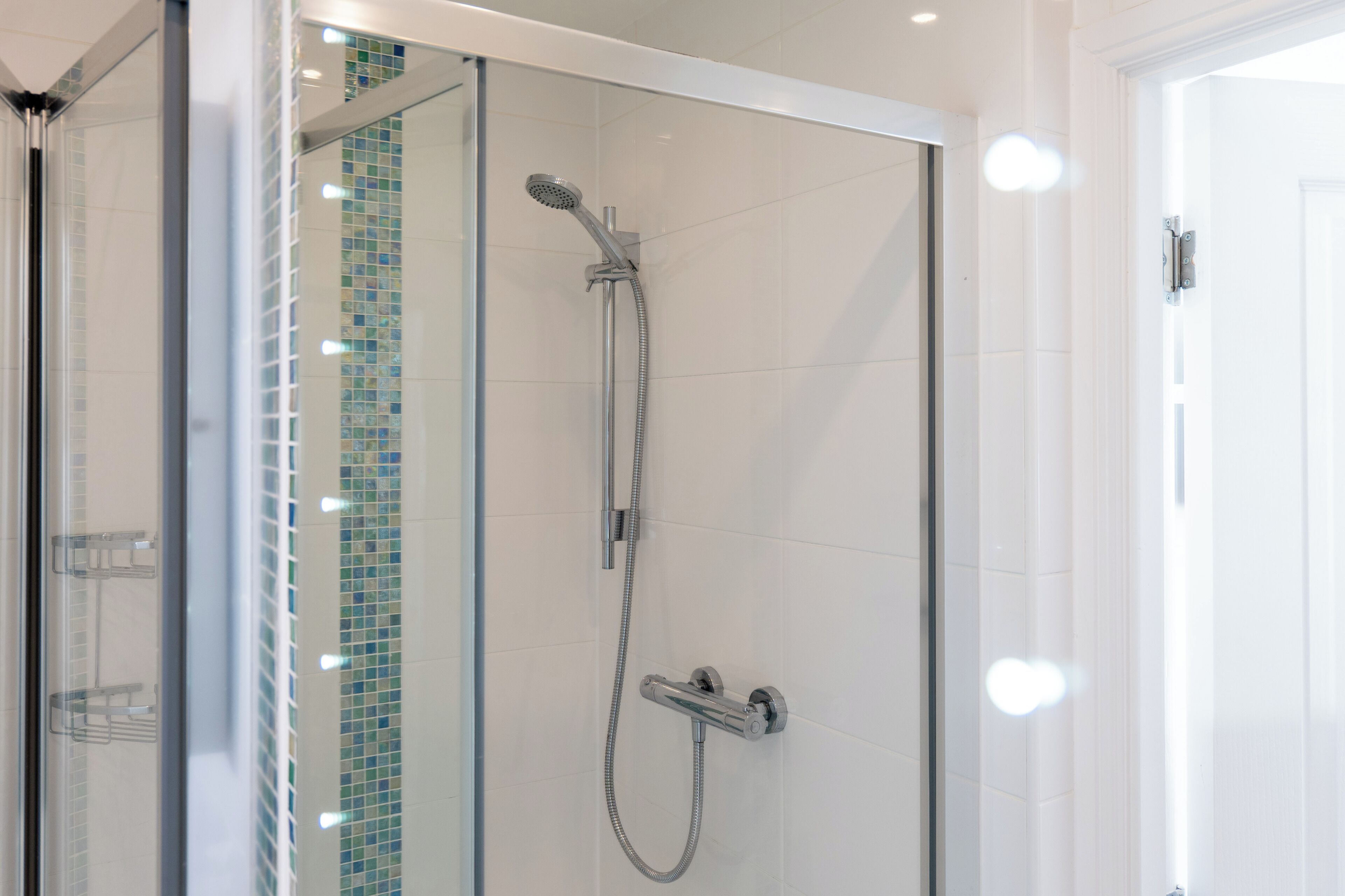 A glass-enclosed shower with a handheld showerhead and a wall-mounted faucet.