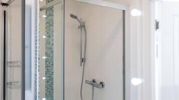 A glass-enclosed shower with a handheld showerhead and a wall-mounted faucet.