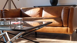 A brown leather sofa, a glass coffee table, and a tripod stand with a telescope. - The Lookout - Donnini Apartments (Prestwick)