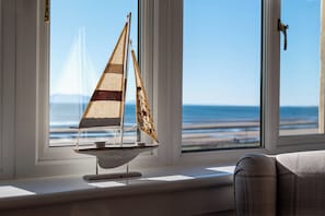 A model sailboat on a windowsill with a view of the beach and ocean.