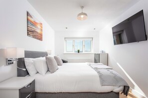 A modern bedroom with a bed, bedside table, TV, and a window.