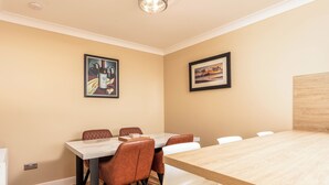 A dining area with a table and chairs, framed artwork on the walls, and a wooden floor. - The Lookout - Donnini Apartments (Prestwick)