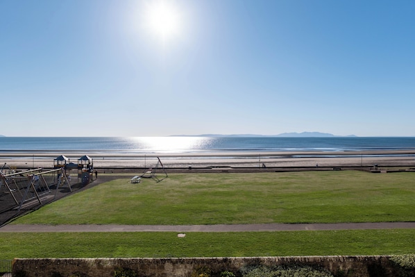 A grassy area with a playground and a view of the beach and ocean.