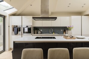 A modern kitchen with a central island, built-in appliances, and a large window. - The Glazed Gable & Alfresco (London)