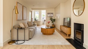 Ein modernes Wohnzimmer mit einer Couch, einem runden Couchtisch, einem Fernseher, einem Kamin und Kunstwerken an den Wänden.