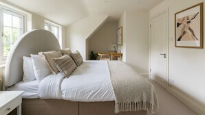 Ein Schlafzimmer mit gebogenem Kopfteil, einem Bett mit weißer Bettwäsche, einem Nachttisch, einem Schreibtisch und einem Stuhl.