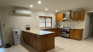 Une cuisine avec des meubles en bois, un four encastré, un distributeur d’eau et un panneau indiquant que des œufs frais sont disponibles.
