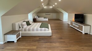 Une chambre spacieuse située dans les combles, avec un grand lit, un canapé, une télévision et un plancher en bois.