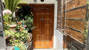 A narrow entrance with a wooden door, a metal gate, and a small garden area with potted plants and flowers. - Elvora Heights BCS New Shimla (Shimla)