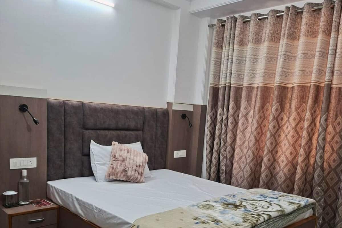 A bedroom with a bed, nightstands, a bedside lamp, a patterned curtain, and a tiled floor.