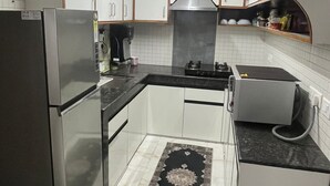 A compact kitchen with white cabinets, a stainless steel refrigerator, a gas stove, and a microwave. - Elvora Heights BCS New Shimla (Shimla)