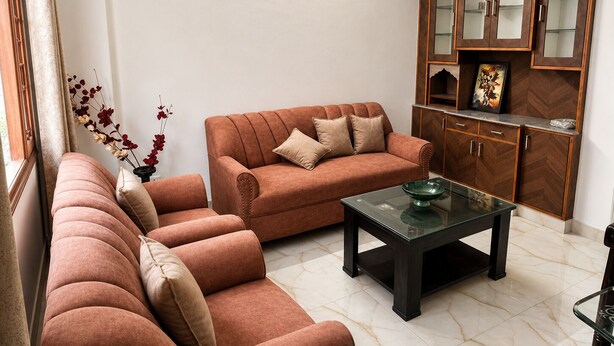 A living room with a sofa set, a coffee table, and a wooden cabinet with glass doors. - Elvora Heights BCS New Shimla (Shimla)