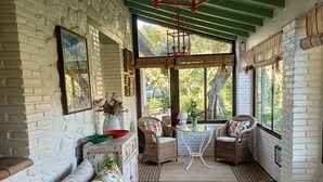 Una habitación con suelo de espiga, un sofá con cojines estampados, sillas de mimbre y un farol colgante rojo.
